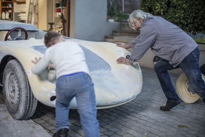 Senior man and boy pushing old car back in garage