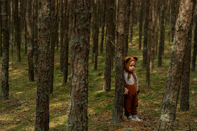 Toddler baby boy in bear bonnet standing in the woods