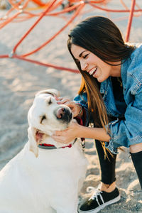 Cheerful woman petting dog at playground during sunset