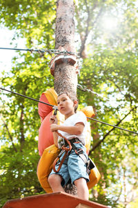 Low angle view of boy on obstacle course in forest