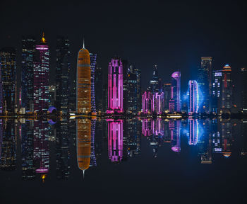 Illuminated modern buildings by river against sky at night/in qatar 