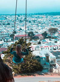 Rear view of woman swinging against cityscape