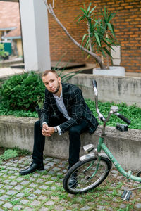 Full length portrait of young man with bicycle against plants