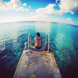 Rear view of woman sitting by sea against cloudy sky