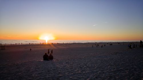 Silhouette people on beach against sky during sunset