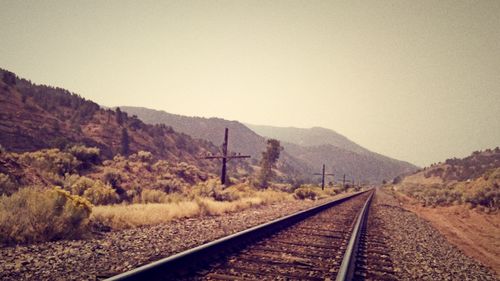 Railroad track by mountains against clear sky