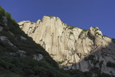 Low angle view of rocky mountain against clear blue sky