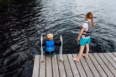 Rear view of children standing on jetty over lake