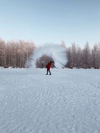Woman playing with snow on land against clear sky
