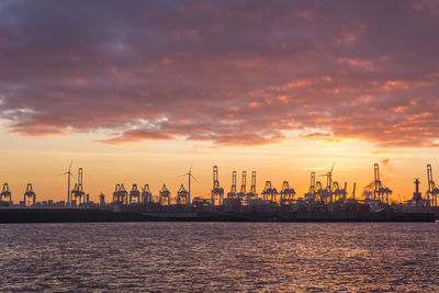 Silhouette of commercial dock against cloudy sky during sunset