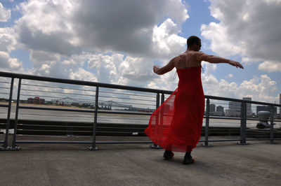 Rear view of man standing by railing against sky