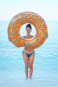 Full length portrait of young woman standing against sea