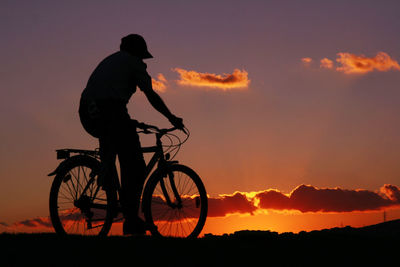 Silhouette man riding bicycle against sky during sunset