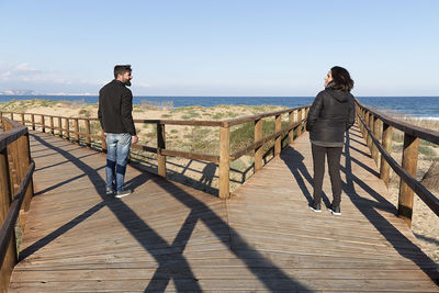 Friends standing on pier at beach against sky