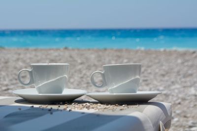 Coffee cup on bed at beach against sky