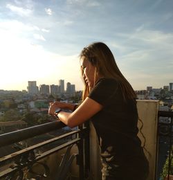 Side view of woman standing at balcony against buildings in city