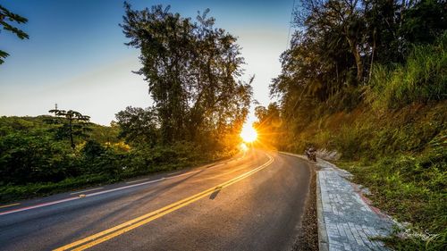 Road amidst trees against sky during sunset