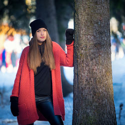 Portrait of young beautiful woman wearing warm clothing standing by tree during winter