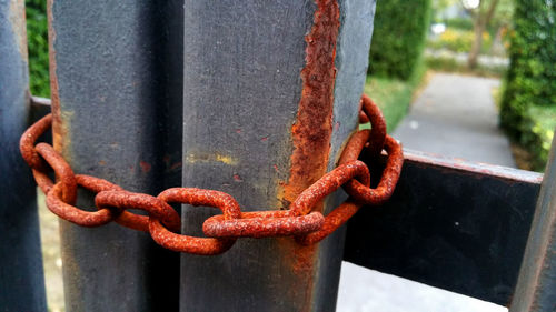 Close-up of rusty chain tied up on metal railing