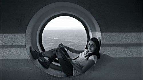 Portrait of woman resting on circular window against sea