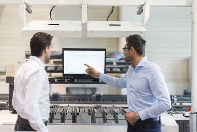 Two businessmen talking at screen in modern factory