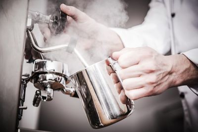 Cropped image of barista steaming milk at cafe