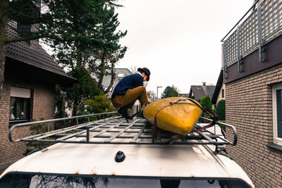 Young man crouching on car roof