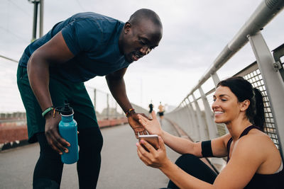 Female athlete smiling while showing mobile phone to sportsman on footbridge