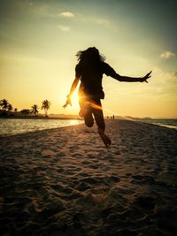 Silhouette girl jumping at beach against sky during sunset
