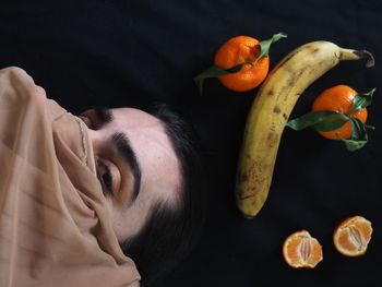 Portrait of man with orange fruit against black background