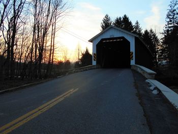 Road passing through bare trees at sunset