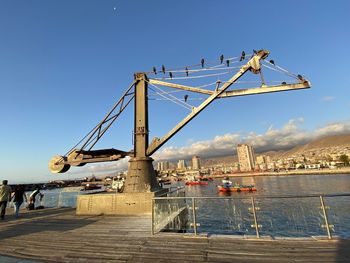 Cranes on bridge over river against sky