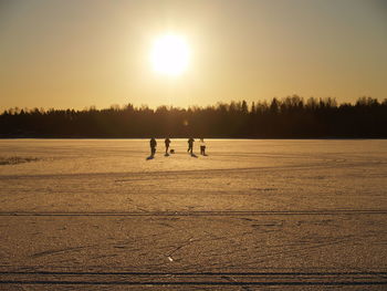 Silhouette people on land against sky during sunset