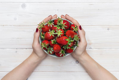 Cropped hands holding strawberries in bowl at table