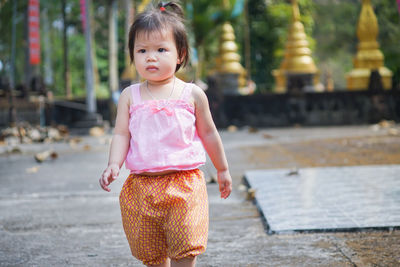 Cute baby girl looking away while walking on footpath