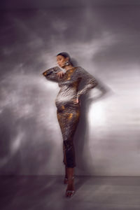 Trendy stylish beautiful pregnant woman in a tight silver sequined dress against a white wall 