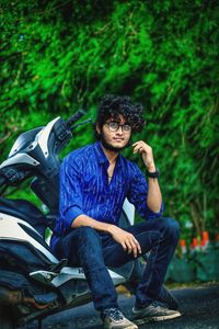 Young man sitting on motor scooter against tree