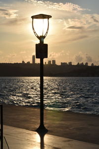 Silhouette street light by sea against sky during sunset