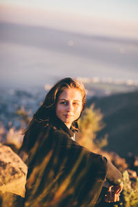 Young woman sitting on mountain against sky during sunset