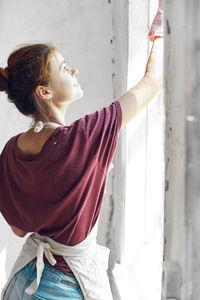 Side view of young woman looking through window