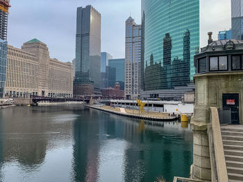 Modern buildings by river against sky in city