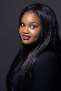 Close-up portrait of smiling young woman against black background