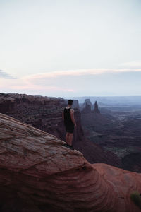 Rear view of man standing on rock against sky
