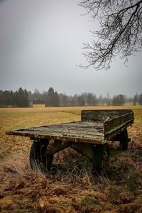Empty bench on field against sky