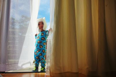 Full length of cute boy holding curtain while standing on balcony