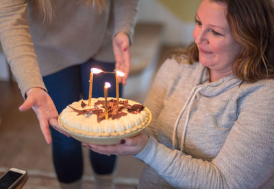 Midsection of woman giving lit birthday cake to friend at home