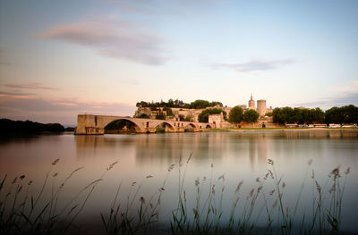 Arch bridge over river by buildings against sky during sunset