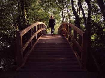 Rear view of woman walking on wooden footbridge amidst trees