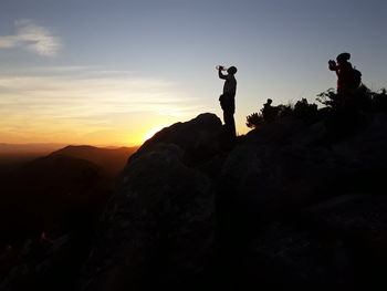 Silhouette man standing on rock against sky during sunset