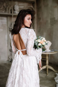 Rear view of bride holding bouquet standing indoors